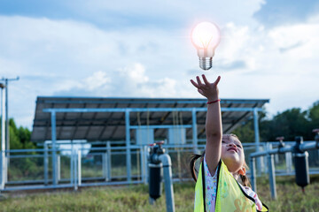A girl with the future of renewable energy and sustainable energy. holding a light bulb in their hand at the solar panel solar farm Environmentally friendly concept and pure energy.
