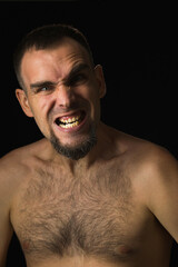 Fototapeta premium Portrait of an angry man with open mouth and frowning eyebrow. Caucasian man with shirtless beard on black background. Human emotions.