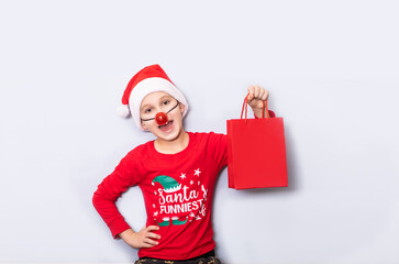 Cute caucasian kid teen boy in red Santa's hat and nose holding red paper bag empty copy space for design or text. Banner. Christmas mockup template.