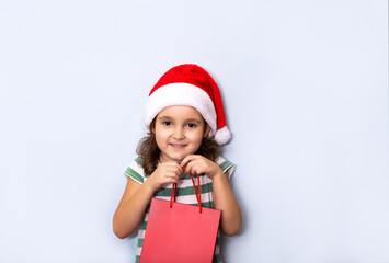 Cute caucasian kid girl in red Santa's hat holding red paper bag empty copy space for design or text. Banner. Christmas mockup template.