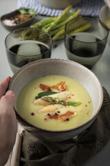 Man hand holding a ceramic bowl full of asparagus cream soup.
