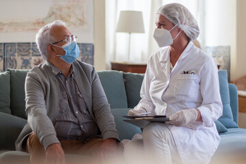 Portrait of Caucasian female doctor visiting old man. Woman in white uniform and man sitting on...