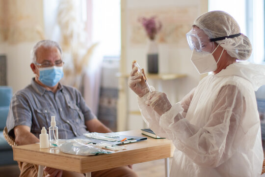 Portrait of female doctor and man preparing for vaccination. Serious woman filling syringe and senior man waiting both wearing masks at home. Health care and vaccination during Covid pandemic concept - Powered by Adobe