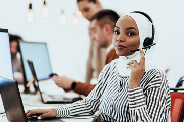 African American muslim woman with hijab and headset working as customer support in a modern office.