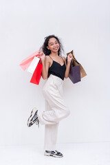 A cheerful young asian woman holding many shopping bags, enjoying a shopping spree. Isolated on a white background.