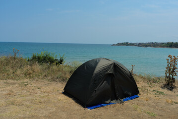 A black tent stands on the ground on the shore of the pure Black Sea on a clear sunny holiday. Active rest in wild nature.