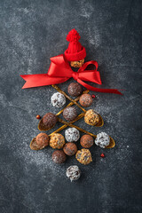 Christmas tree made of chocolate truffles, hazelnuts, anise stars, decorations, spoons and powdered sugar snow on dark background. Christmas holiday card. Holiday food concept for magazine page.