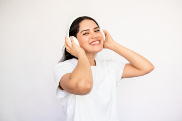 Portrait of happy young woman listening to music in headphones over white background. Caucasian lady wearing white T-shirt looking at camera and smiling. Music and leisure concept