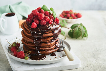 Chocolate Pancakes. Pancakes with fresh raspberry with chocolate glaze or toppings in gray bowl on light gray table background. Homemade classic american pancakes. Page for magazine concept.