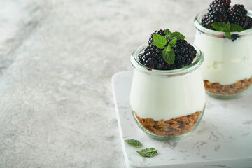 Yogurt with granola, blackberry berry fruits and muesli served in glass jar on gray concrete table background. Healthy breakfast concept. Healthy food for breakfast, top view