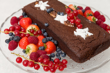 Brownie chocolate cake with fresh blueberries, raspberries, strawberries, white sugar stars and red currant. Home cake decorated with fruits. Festive concept. Selective soft focus