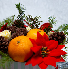 white gift box on a white background with chocolate flowers and two oranges with a red satin ribbon close up