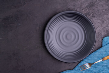 Fototapeta na wymiar Empty black round plate with rehearsal Cloth arranged on the table on a dark moody black background. simple dinner with copy space, top view