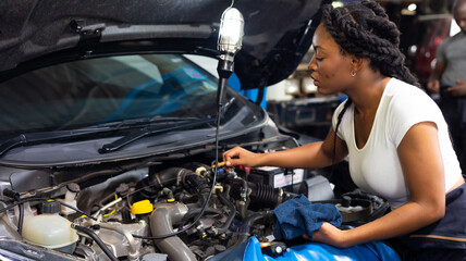 African female auto mechanic worker checking oil level in car engine at Car Service station. Car...