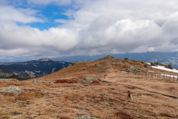 Hiking trail with panoramic view on the alpine pasture of the Saualpe, Lavanttal Alps, Carinthia, Austria, Europe. Trekking on cloudy early spring day. Dry meadow with fence along the pathway