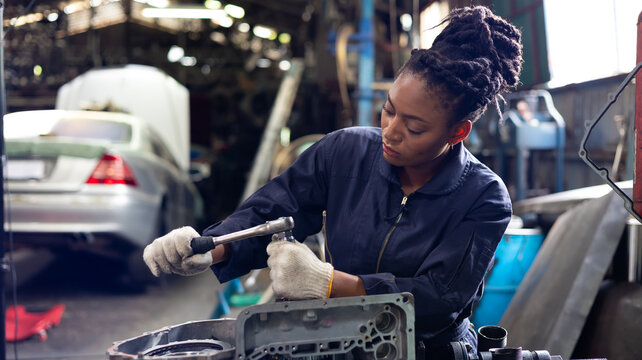 African young female car mechanic checking and fixing car engine at service car garage. Black woman mechanic working in car service and maintenance workshop.
