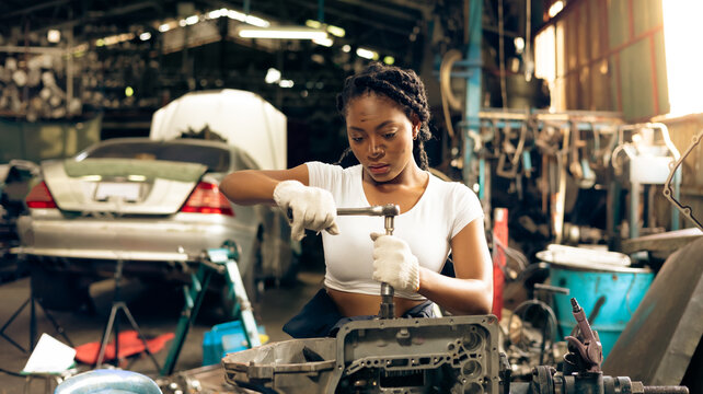 African young female car mechanic checking and fixing car engine at service car garage. Black woman mechanic working in car service and maintenance workshop.