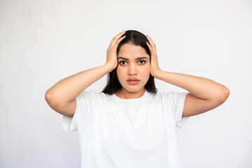 Portrait of worried young woman holding head in hands over white background. Caucasian lady wearing white T-shirt looking at camera in fear. Anxiety or failure concept