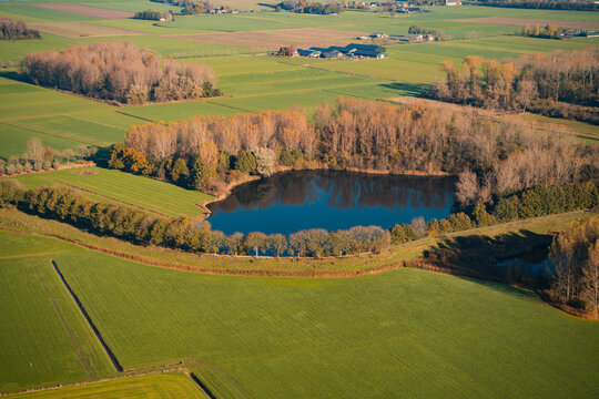 Lake in the farmland, reflecting the sun. Aerial photo