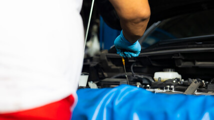 Senior asian male auto mechanic worker checking oil level in car engine at Car Service station. Car maintenance and auto service garage concept.