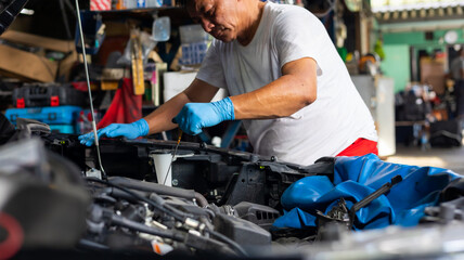 Senior asian male auto mechanic worker checking oil level in car engine at Car Service station. Car...