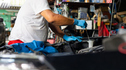 Senior asian male auto mechanic worker checking oil level in car engine at Car Service station. Car maintenance and auto service garage concept.