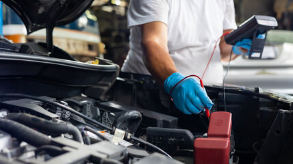 Obraz na płótnie Canvas Senior mechanic man uses multimeter voltmeter to check voltage level in car battery at car service and maintenance garage.
