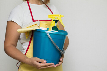 The girl holds a bucket and cleaning products in her hands