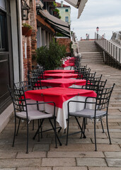 Fototapeta na wymiar Charming restaurant with red tablecloth tables by the water canal in Venice, Italy 