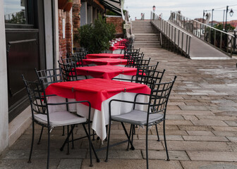 Charming restaurant with red tablecloth tables by the water canal in Venice, Italy 