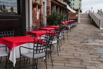 Charming restaurant with red tablecloth tables by the water canal in Venice, Italy 