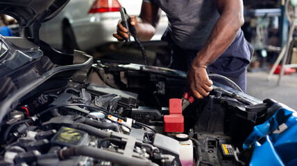African american mechanic man uses  multimeter voltmeter to check voltage level in car battery at...