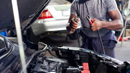 African american mechanic man uses  multimeter voltmeter to check voltage level in car battery at car service and maintenance garage.