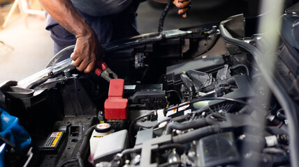 Fototapeta na wymiar African american mechanic man uses multimeter voltmeter to check voltage level in car battery at car service and maintenance garage.
