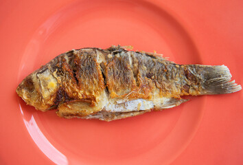 A whole fried carp with a fried crust, served on a bright red plate. View from above.