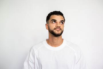 Portrait of confident young man looking away on white background. Bearded man wearing white T-shirt posing with thoughtful expression. Uncertainty and doubt concept