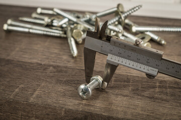 Lot of screws on an old wooden workbench, measured by an vernier caliper.