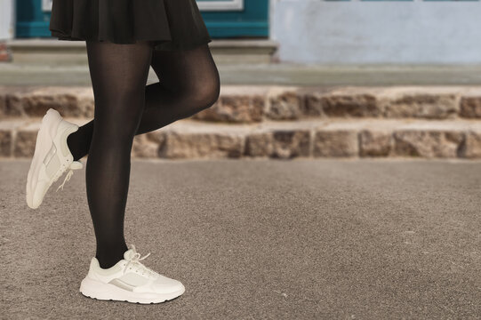 Close-up woman in stylish white sneakers in a black skirt with pantyhose. Fashionable autumn or spring concept.