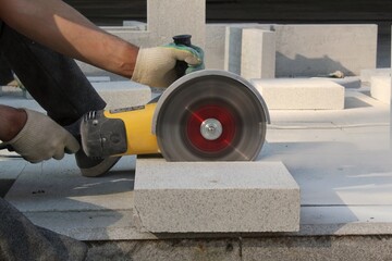 Hands of worker with electric grinder trims paving slabs on the construction site. Concept of...