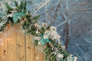Christmas, New Year hut exterior with garland, fur-tree branches and blue flowers on snow-covered forest background