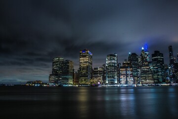 New York City skyline at cloudy night, with city lights and lights reflecting on the water's surface