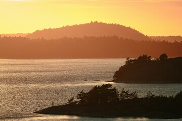Mesmerizing shot of sunset by the sea,a silhouette of mountains on horizon and planty lands in front