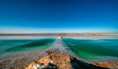 Seascape shot in long exposure, with a clear blue sky and distant mountains in the background