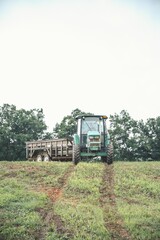 Obraz premium Farm tractor moving on grass farm fields with trees under bright sky, vertical shot