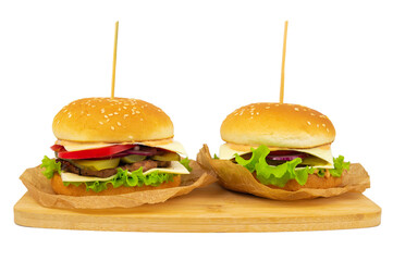 Two hamburgers with beef patty, tomatoes and cheese, laid out on wrapping paper, on a wooden board