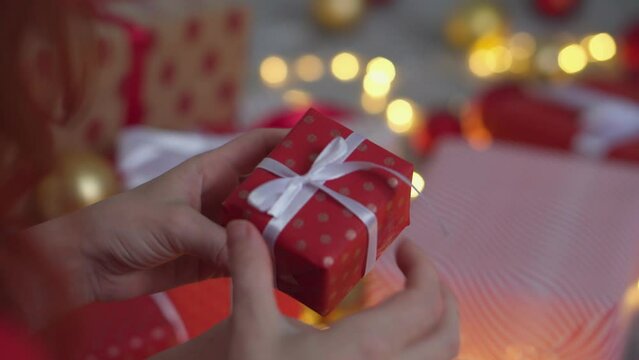 Girl in a Santa hat creates New Year's packages from red wrapping paper. Young woman is packing Christmas presents for her friends and relatives. Decorations, preparation for the winter holiday season