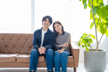 ソファに座り微笑む夫婦-明るい観葉植物のあるリビング