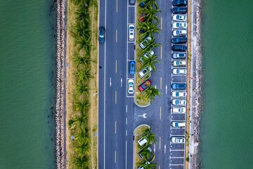 Top view of cars parked in an open-air parking lot surrounded by palm trees and water