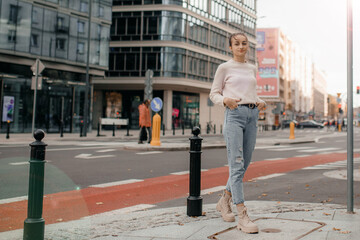 Cool girl in sweater looks away. Lifestyle portrait of a young stylish woman walking outdoors. Walk in Warsaw. Lifestyle portrait of a young woman in sweater standing on the street in Warsaw.