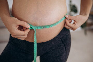 Pregnant woman measuring belly with measuring tape